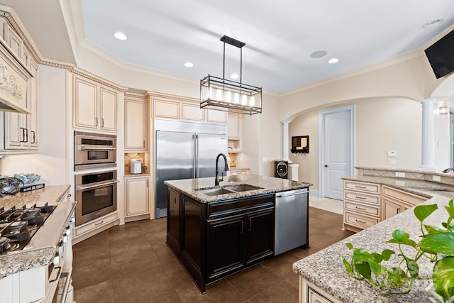 kitchen with cream cabinetry, an island with sink, a sink, arched walkways, and appliances with stainless steel finishes