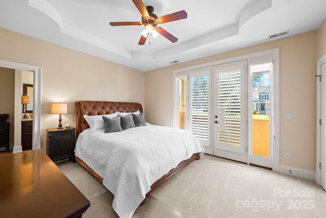 bedroom with visible vents, light colored carpet, a tray ceiling, and access to outside