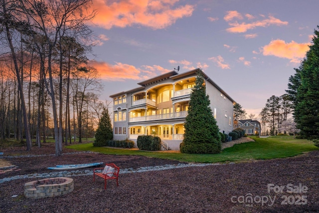 back of house with a lawn, a fire pit, a balcony, and stucco siding