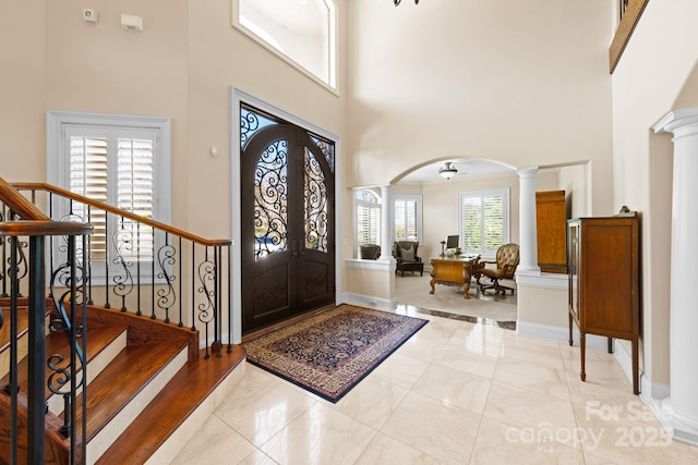 entrance foyer with baseboards, stairs, decorative columns, a high ceiling, and arched walkways