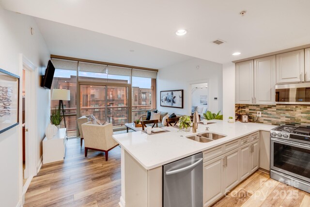 kitchen with sink, appliances with stainless steel finishes, backsplash, light hardwood / wood-style floors, and kitchen peninsula