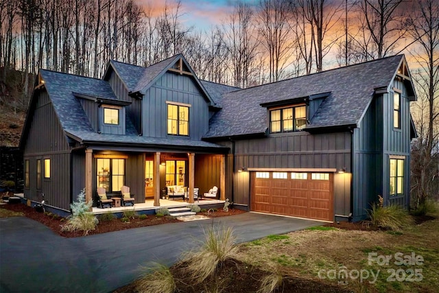 modern farmhouse featuring a garage, driveway, a shingled roof, covered porch, and board and batten siding