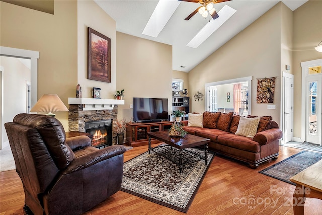 living room featuring a skylight, high vaulted ceiling, hardwood / wood-style flooring, ceiling fan, and a fireplace