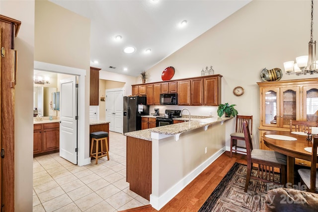 kitchen with a kitchen bar, a chandelier, kitchen peninsula, pendant lighting, and black appliances