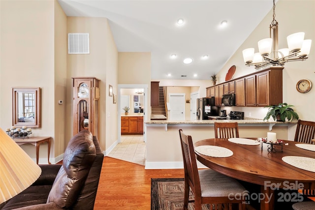 dining space with light hardwood / wood-style floors, high vaulted ceiling, and a notable chandelier