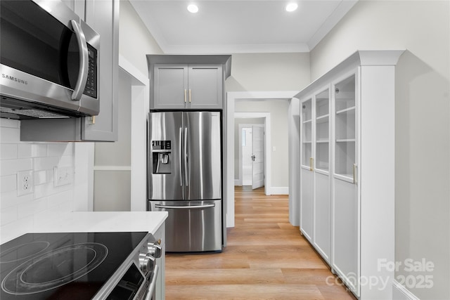 kitchen featuring crown molding, gray cabinets, backsplash, stainless steel appliances, and light wood-type flooring