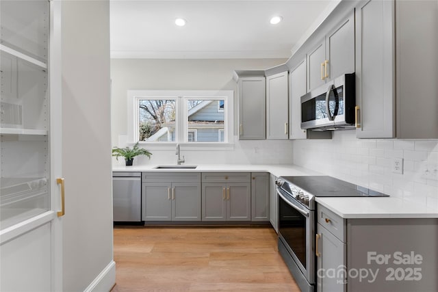 kitchen with sink, gray cabinetry, light hardwood / wood-style flooring, appliances with stainless steel finishes, and backsplash