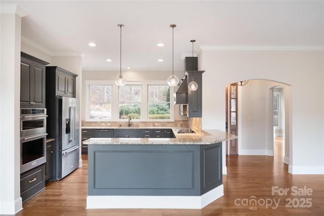 kitchen with crown molding, hanging light fixtures, stainless steel appliances, light stone countertops, and hardwood / wood-style floors