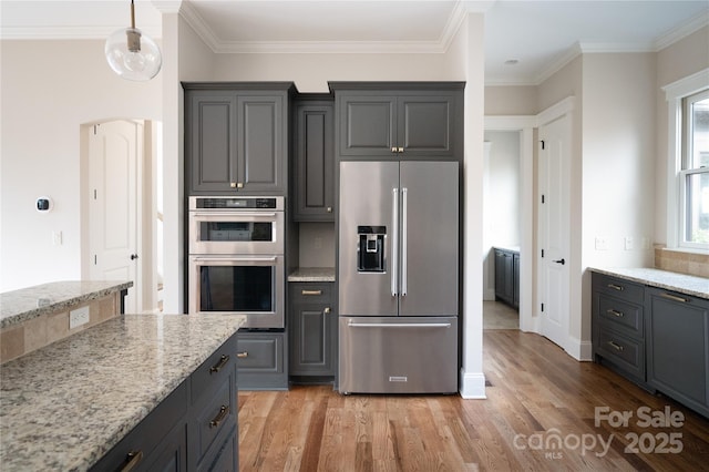 kitchen with stainless steel appliances, light stone countertops, pendant lighting, and light hardwood / wood-style flooring