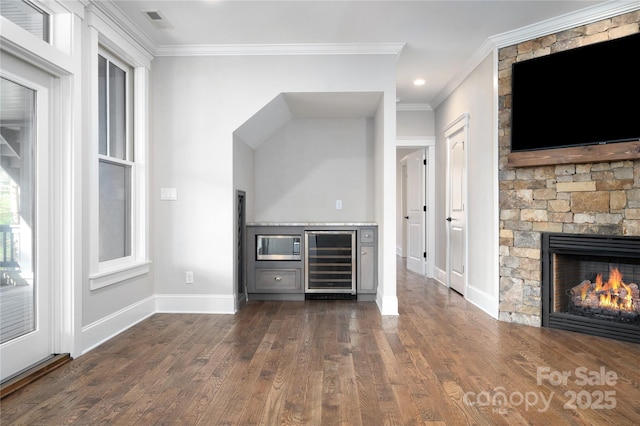 unfurnished living room featuring wine cooler, ornamental molding, dark hardwood / wood-style flooring, and a stone fireplace