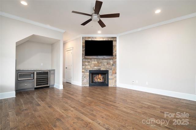 unfurnished living room with crown molding, dark wood-type flooring, ceiling fan, wine cooler, and a fireplace