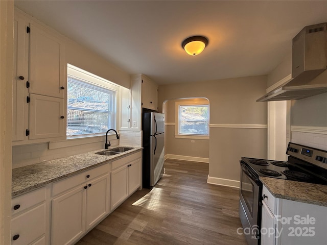 kitchen with sink, stainless steel appliances, light stone counters, white cabinets, and wall chimney exhaust hood