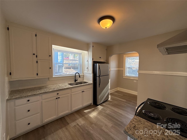 kitchen featuring stainless steel refrigerator, white cabinetry, sink, light stone counters, and light wood-type flooring