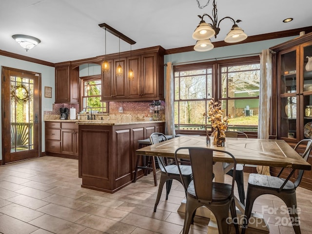 kitchen with backsplash, a chandelier, hanging light fixtures, light stone counters, and crown molding