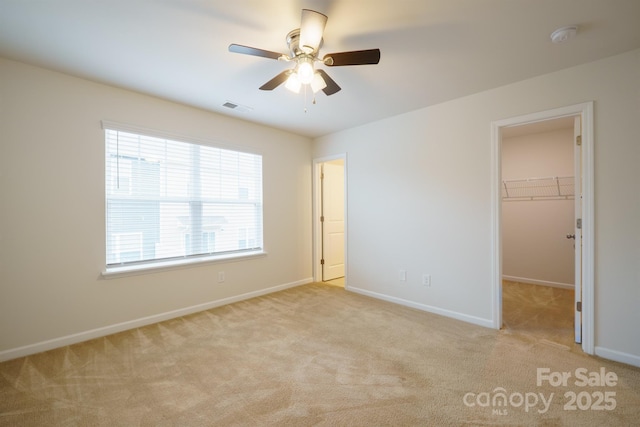 unfurnished bedroom with light carpet, a walk in closet, a closet, and ceiling fan