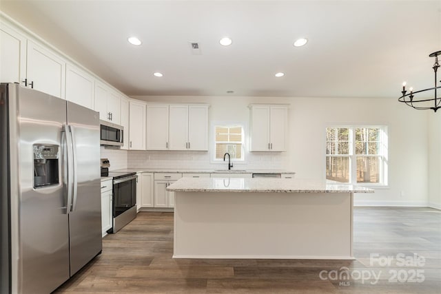 kitchen with hanging light fixtures, appliances with stainless steel finishes, a kitchen island, light stone countertops, and white cabinets