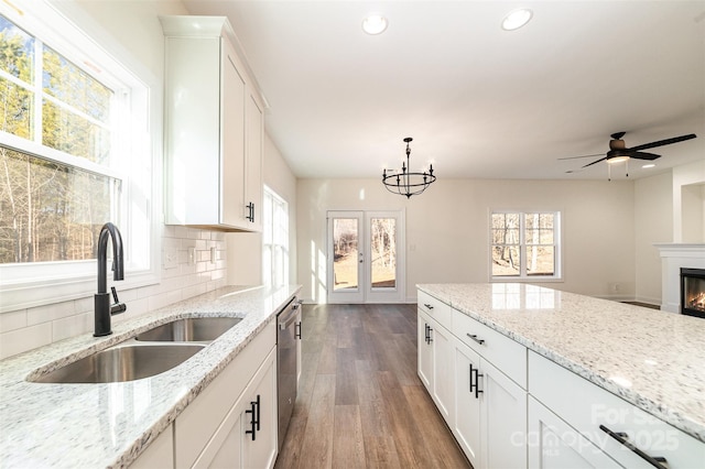 kitchen with white cabinetry, light stone counters, sink, and hanging light fixtures