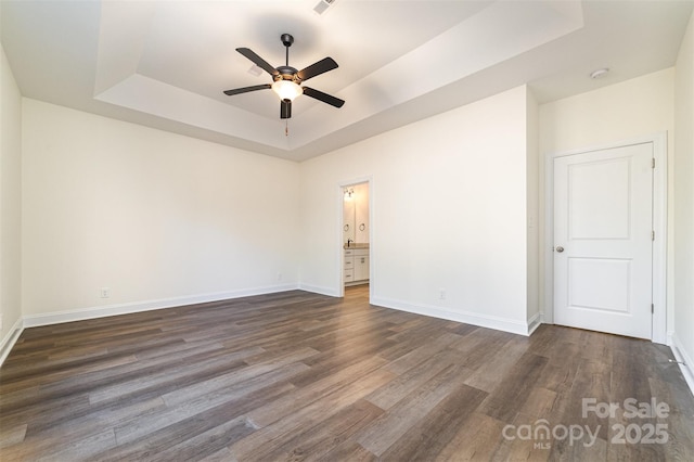 empty room with ceiling fan, dark hardwood / wood-style floors, and a raised ceiling