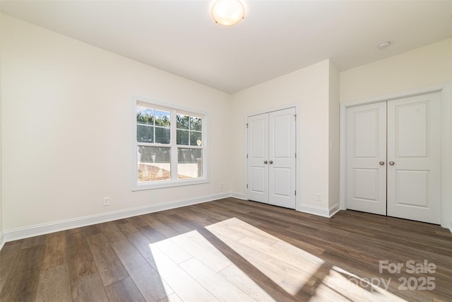 unfurnished bedroom with dark hardwood / wood-style flooring and two closets