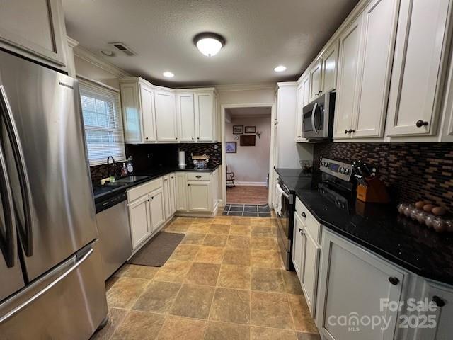 kitchen with sink, tasteful backsplash, ornamental molding, appliances with stainless steel finishes, and white cabinets