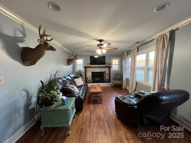 living room with dark hardwood / wood-style flooring, crown molding, a tile fireplace, and ceiling fan