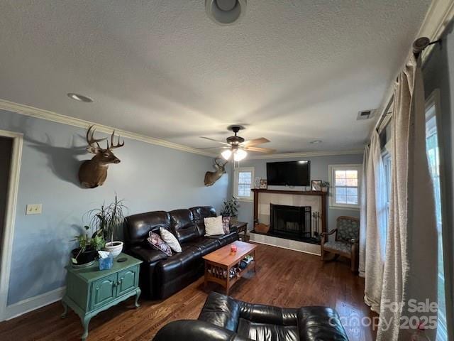 living room featuring crown molding, ceiling fan, dark hardwood / wood-style floors, a fireplace, and a textured ceiling