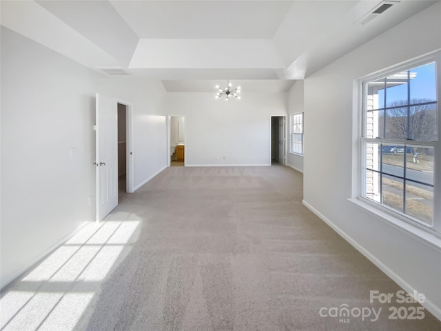 carpeted spare room with a tray ceiling and a notable chandelier