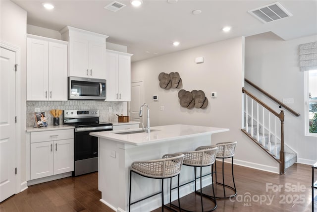 kitchen with sink, a kitchen island with sink, stainless steel appliances, tasteful backsplash, and white cabinets