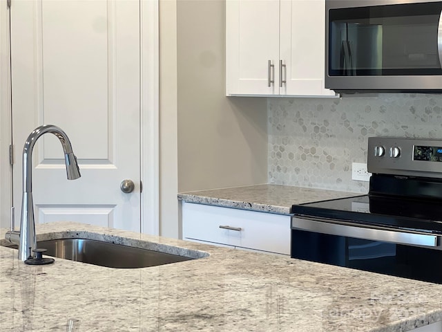 kitchen with a sink, white cabinetry, appliances with stainless steel finishes, light stone countertops, and tasteful backsplash