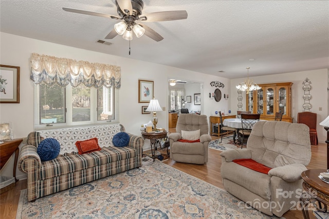 living room with ceiling fan with notable chandelier, a textured ceiling, and light wood-type flooring