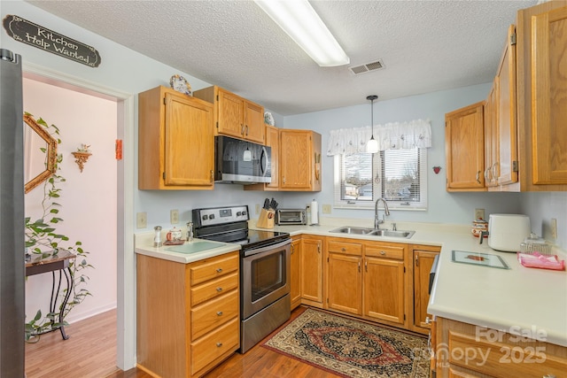 kitchen with sink, a textured ceiling, light wood-type flooring, appliances with stainless steel finishes, and pendant lighting