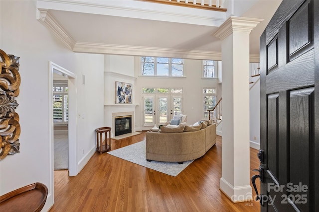 living room featuring ornate columns, a towering ceiling, crown molding, light wood-type flooring, and french doors