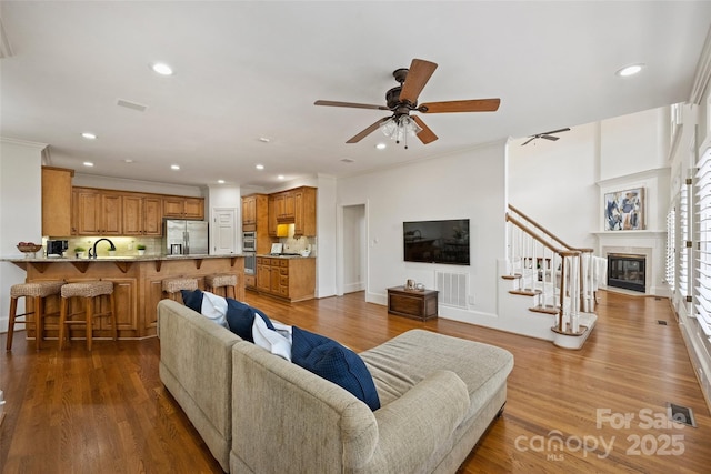 living room with crown molding, sink, hardwood / wood-style flooring, and ceiling fan