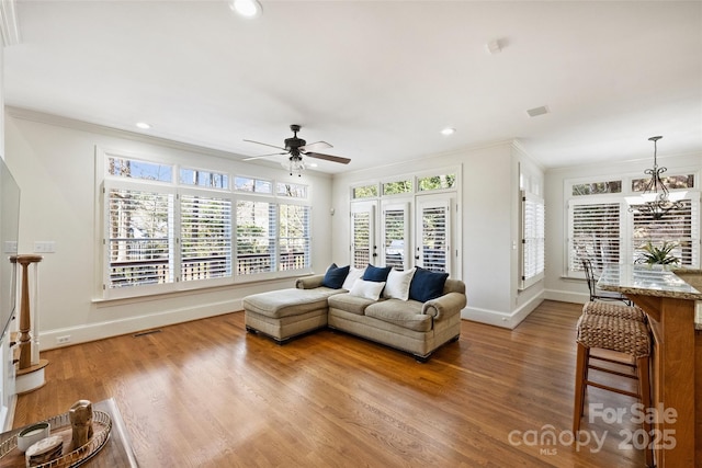 living room featuring hardwood / wood-style floors, crown molding, and ceiling fan with notable chandelier