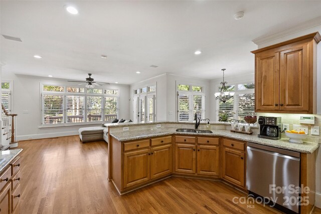 kitchen with sink, hanging light fixtures, stainless steel dishwasher, light stone counters, and light hardwood / wood-style floors