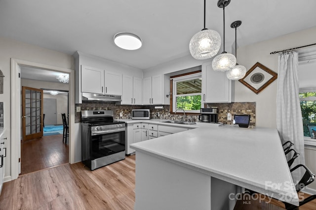 kitchen with a peninsula, a sink, under cabinet range hood, appliances with stainless steel finishes, and light wood-type flooring