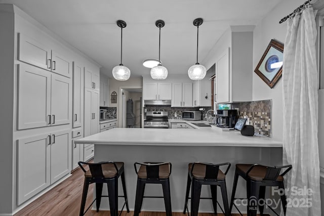 kitchen featuring a breakfast bar, white cabinetry, kitchen peninsula, stainless steel appliances, and backsplash