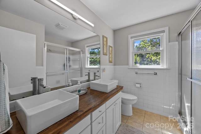 bathroom with tile patterned floors, a shower with door, vanity, and tile walls