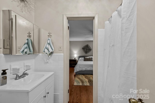 ensuite bathroom with ensuite bath, wood finished floors, tile walls, wainscoting, and vanity