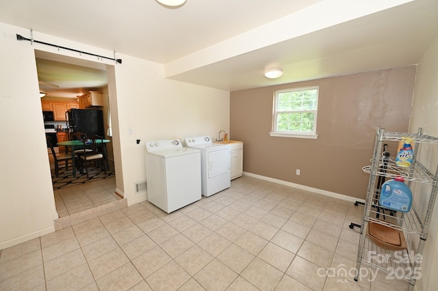 laundry room featuring a barn door, washer and clothes dryer, and light tile patterned floors