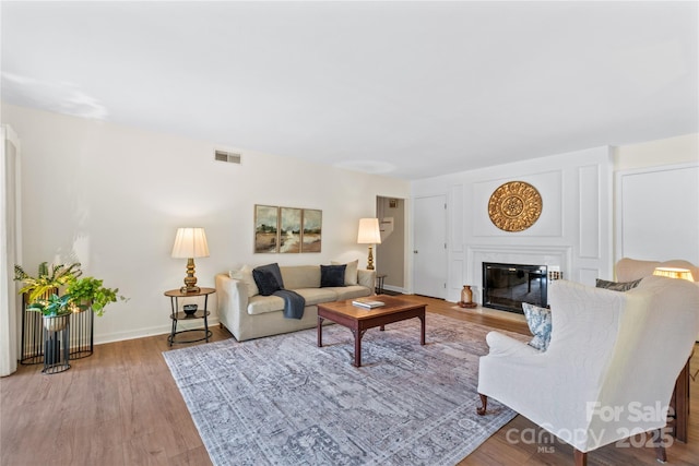 living area with baseboards, a fireplace with flush hearth, visible vents, and wood finished floors