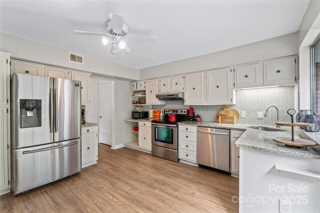 kitchen featuring visible vents, stainless steel appliances, under cabinet range hood, open shelves, and a sink