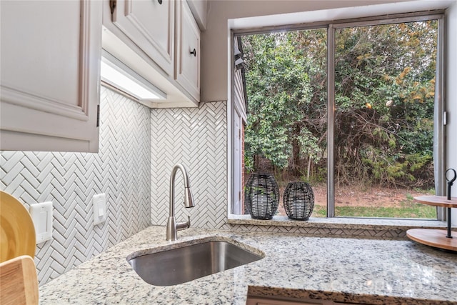 kitchen featuring light stone counters, backsplash, a sink, and white cabinetry