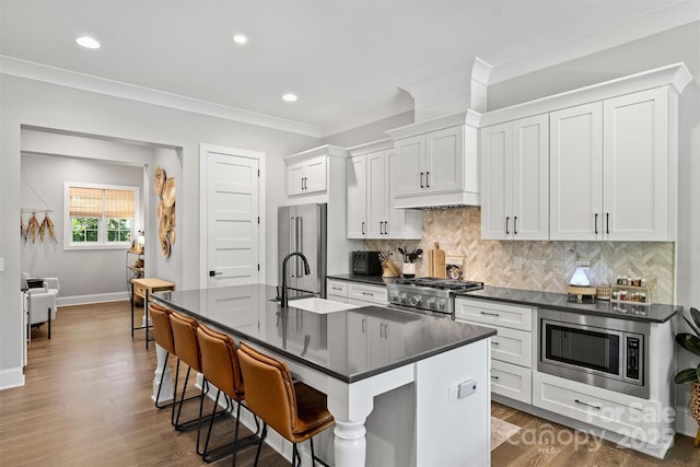 kitchen featuring sink, white cabinetry, a center island with sink, stainless steel appliances, and a kitchen bar