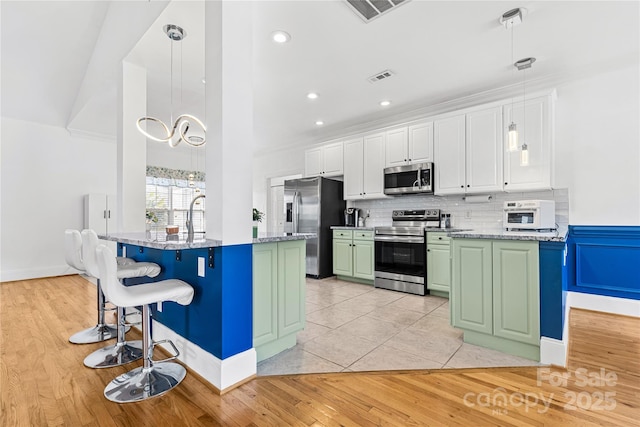 kitchen featuring pendant lighting, a breakfast bar area, green cabinets, white cabinetry, and appliances with stainless steel finishes