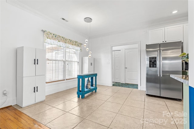 kitchen with light tile patterned floors, crown molding, stainless steel fridge, white cabinets, and decorative light fixtures