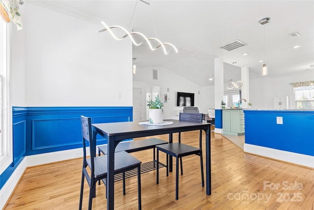 dining space with lofted ceiling, ceiling fan with notable chandelier, and light hardwood / wood-style flooring