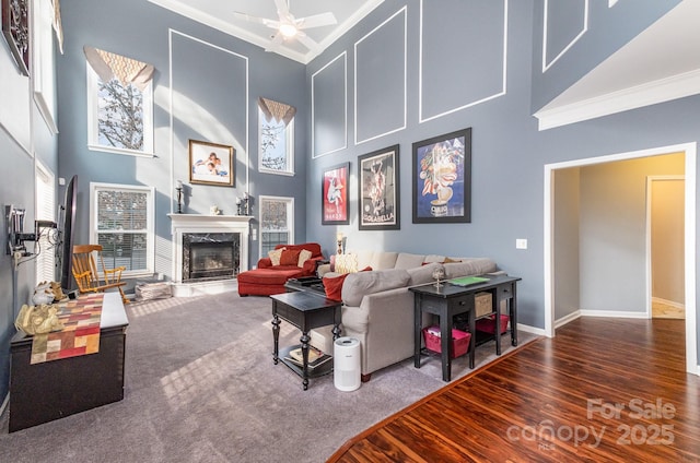 living room featuring a high ceiling, ornamental molding, dark carpet, ceiling fan, and a high end fireplace