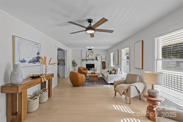 living room with ceiling fan, a fireplace, and light wood-type flooring