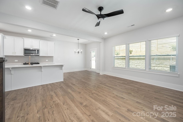 unfurnished living room featuring ceiling fan with notable chandelier and light wood-type flooring